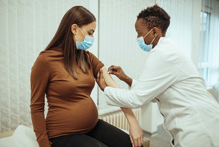 This image has an empty alt attribute; its file name is Pregnant_woman_with_mask_getting_vaccine_resized.jpg